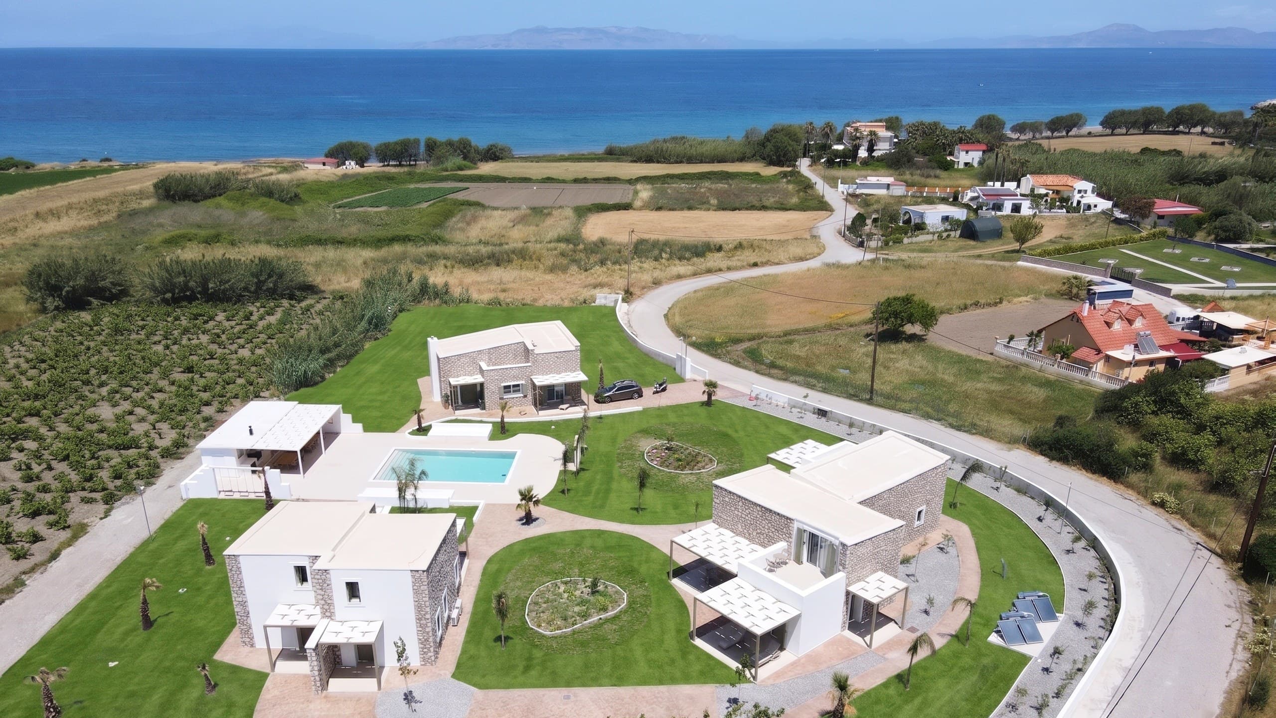 Drone view of the whole resort — four houses, the pool and the garden, with the Aegean beyond